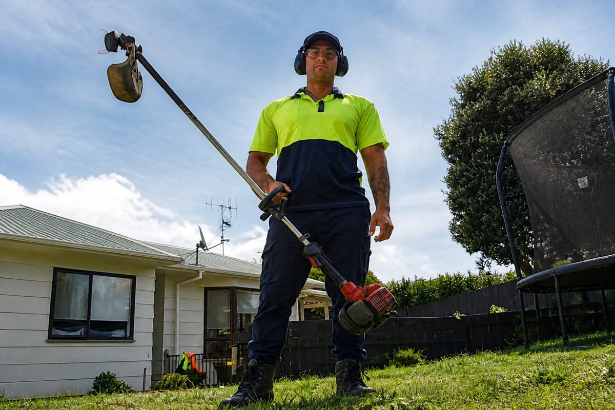 George Stott trimming a Kapiti Coast lawn in hi-vis and earmuffs